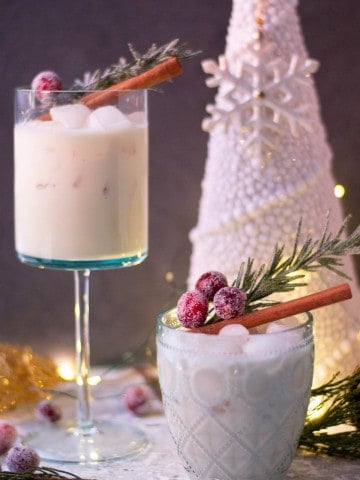 Ponche-Crema-served-in-pretty-glasses-with-festive-garnishes-and-light-color-christmas-decorations-and-white-christmas-tree-in-background