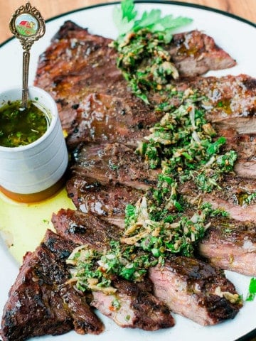 kirt steak with chimichurri sauce drizzled and over a white place