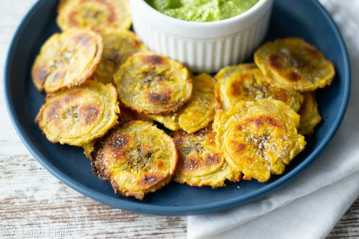 Oven-Baked-tostones-(Crispy-Baked-Green-Plantains)-on-blue-plate-with-peruvian-aji-verde-green-sauce