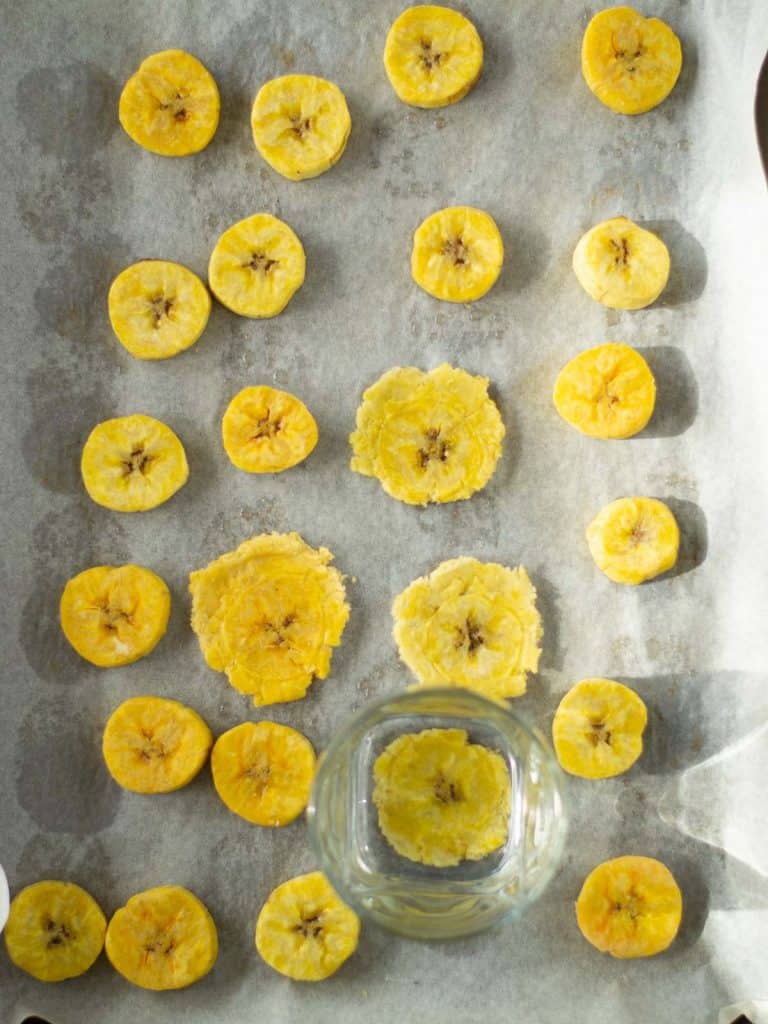 smashing-green-plantains-slices-on-a-sheet-pan-with-a-glass-for-tostones