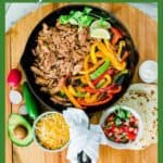 fajita filling ingredients in cast iron skillet with toppings on the side