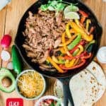 fajita filling ingredients in cast iron skillet with toppings on the side