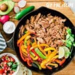 fajita filling ingredients in cast iron skillet with toppings on the side