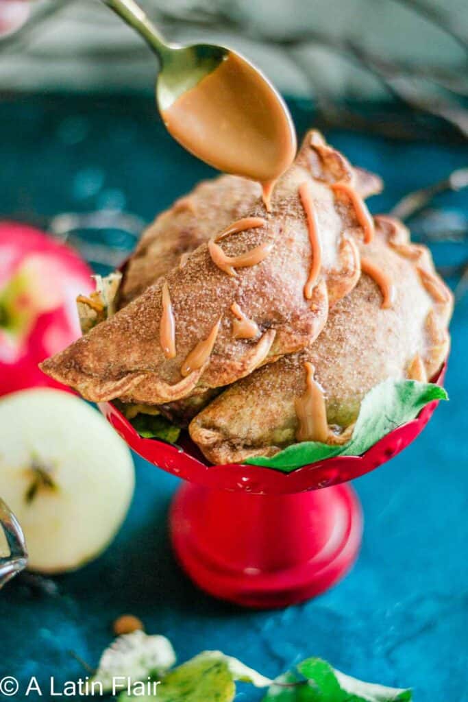 apple Empanadas served on a red stand and drizzled with dulce de leche