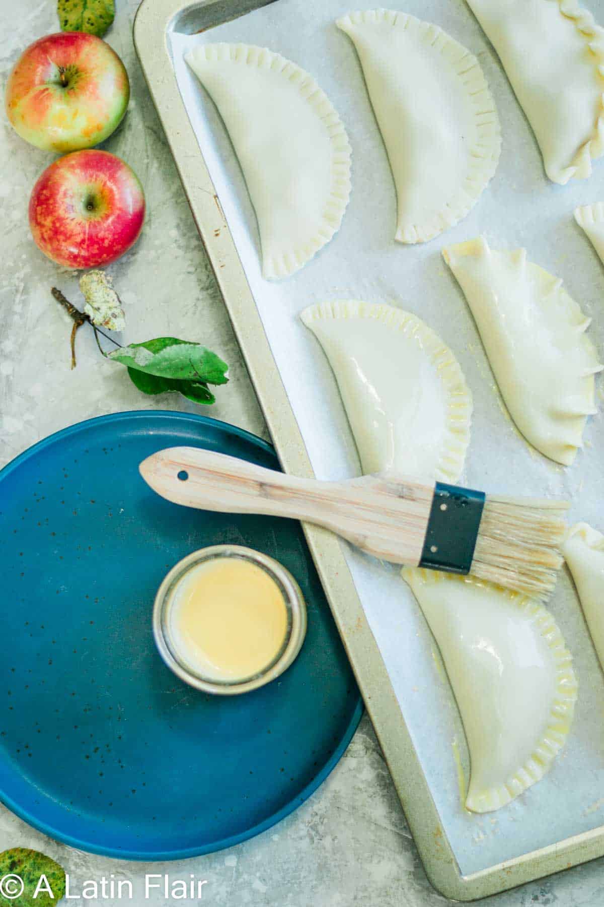 Brushing the tops of fruit filled empanadas with egg wash 