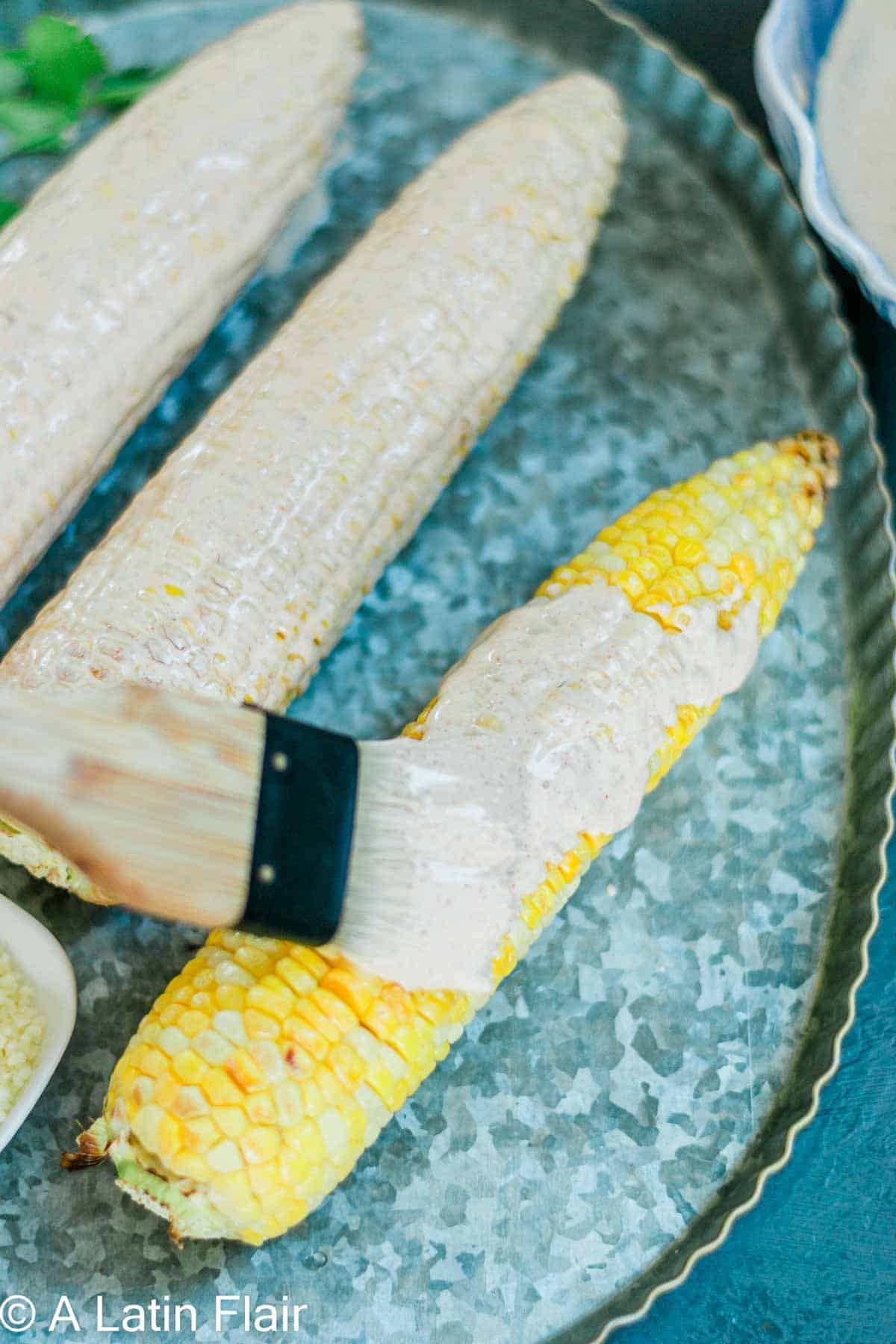 brushing mexican street corn with mexican crema