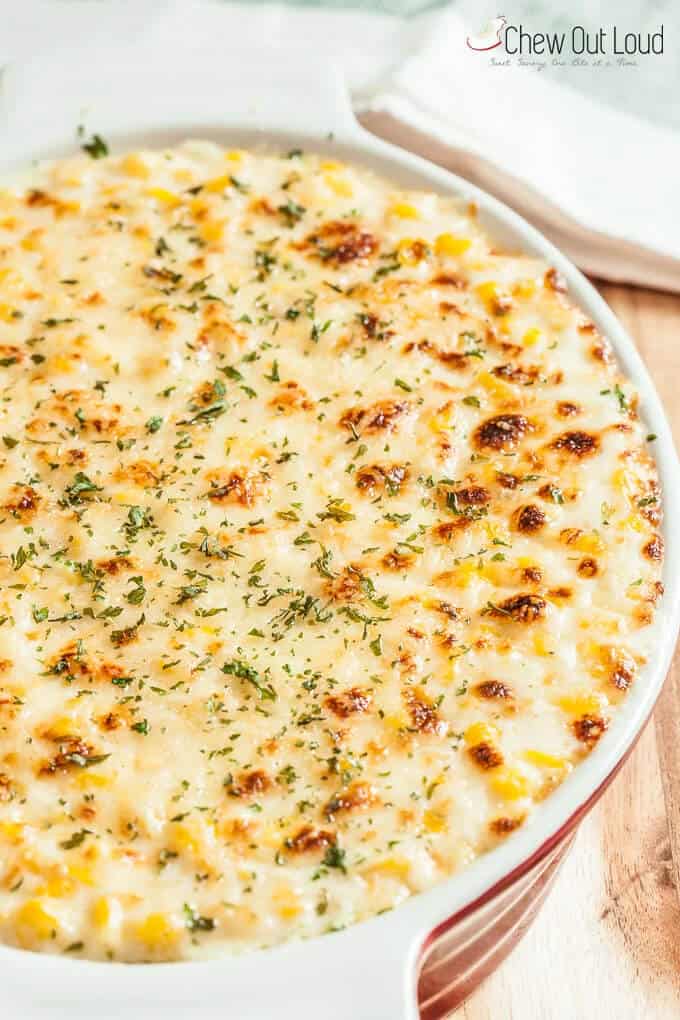 Creamy baked corn casserole with a golden, crispy top and sprinkled with green herbs in a white baking dish on a wooden surface. Warm and inviting.