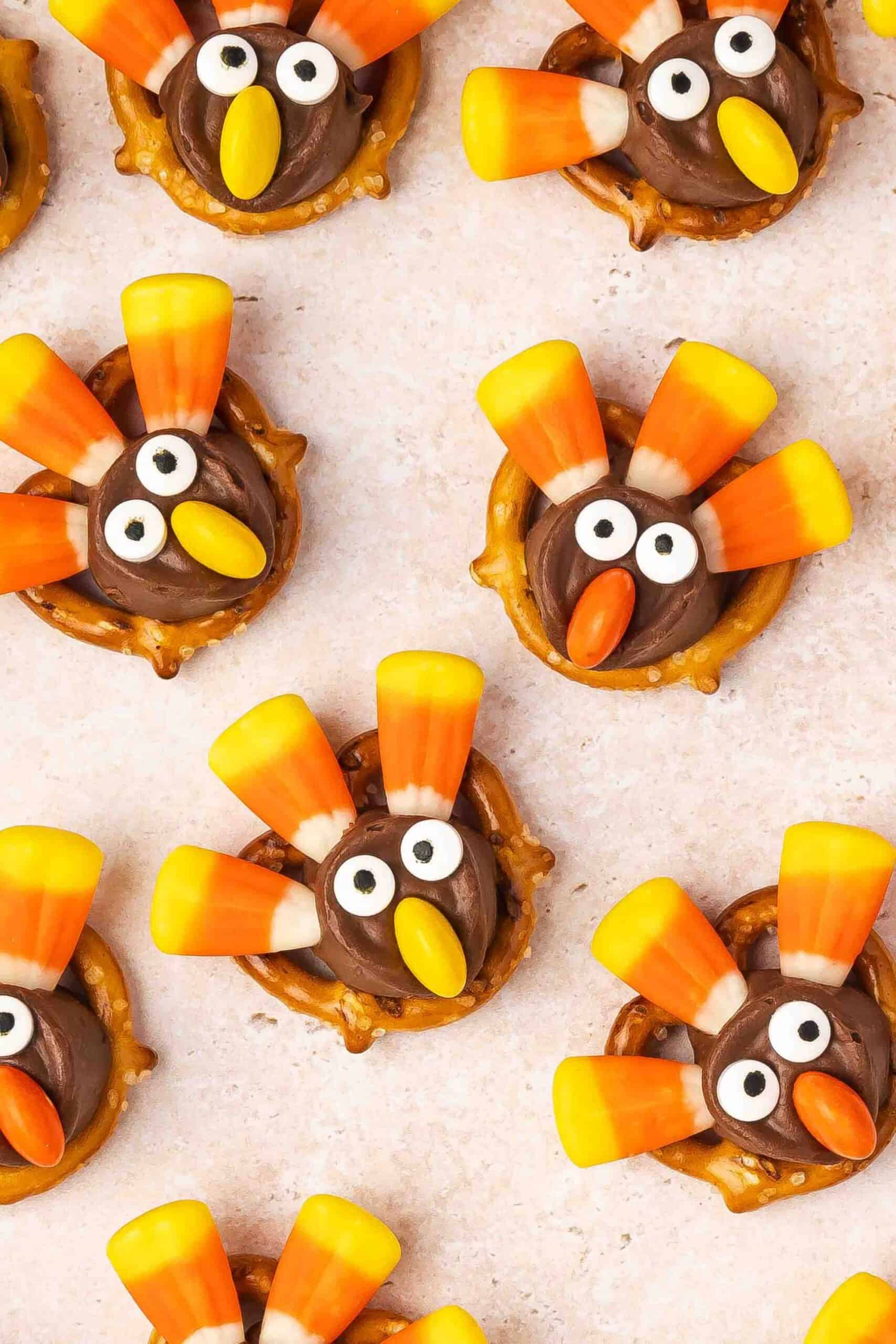 Whimsical turkey-themed treats made from pretzels, candy corn feathers, chocolate bodies, and candy eyes, arranged in a playful pattern on a light surface.