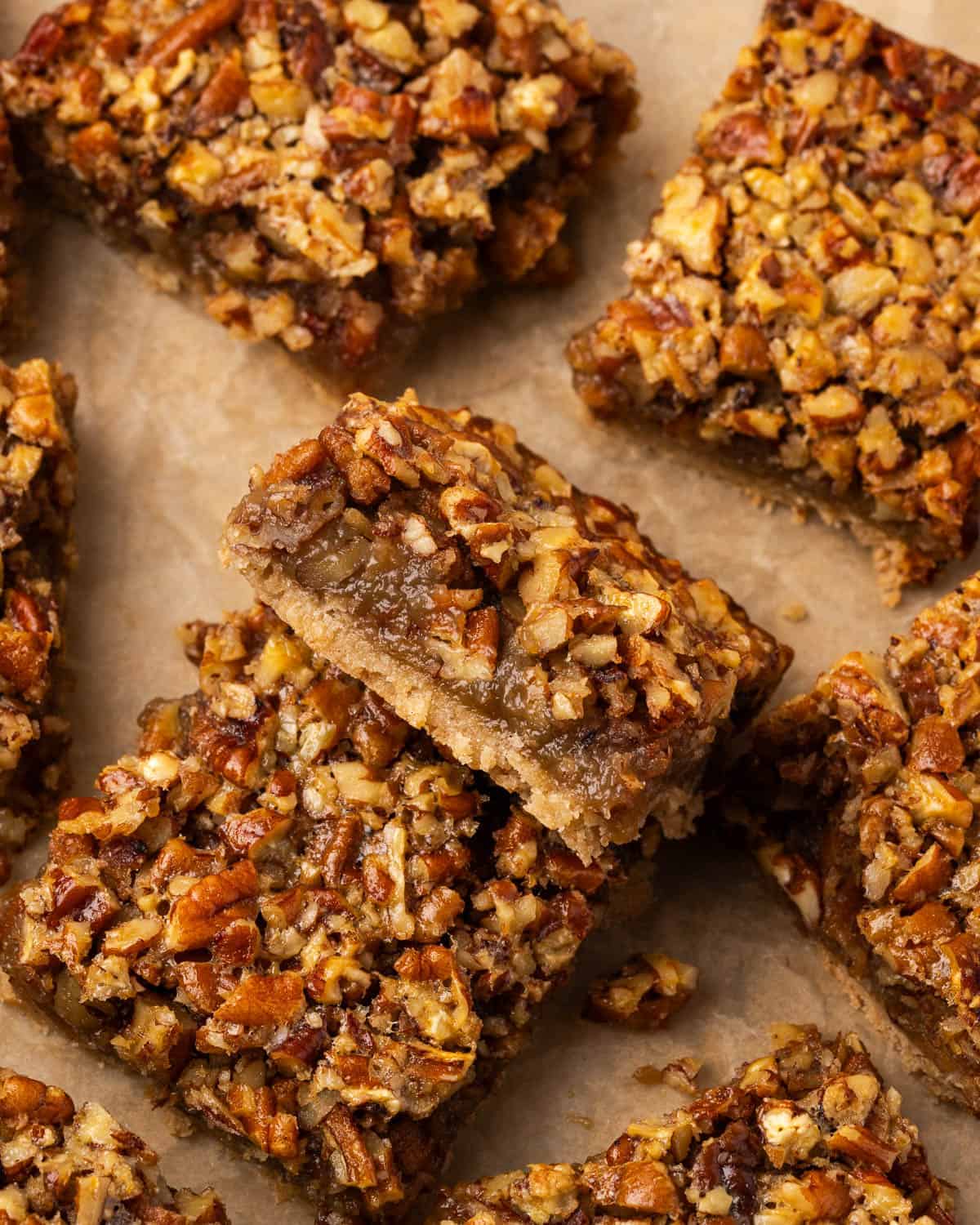 Close-up of pecan bars on parchment paper, featuring a crumbly crust and a caramelized, nutty topping. The bars look rich and indulgent.
