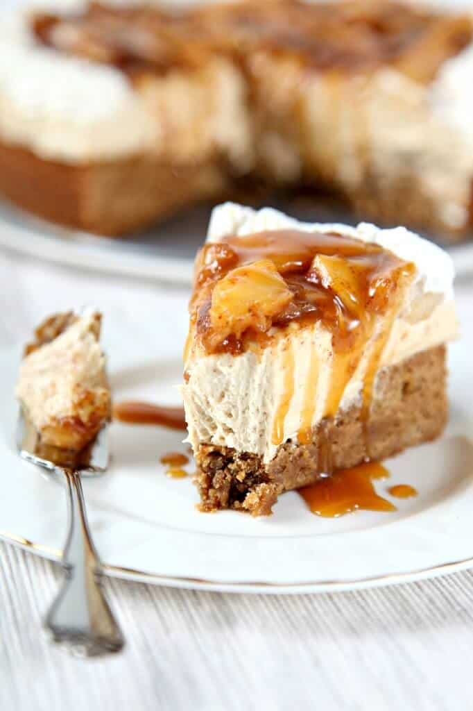 A square slice of layered pumpkin dessert with creamy topping on a white plate. Nearby are decorative mini pumpkins and a glass dish with more dessert. Bright, warm lighting conveys a cozy autumn feel.