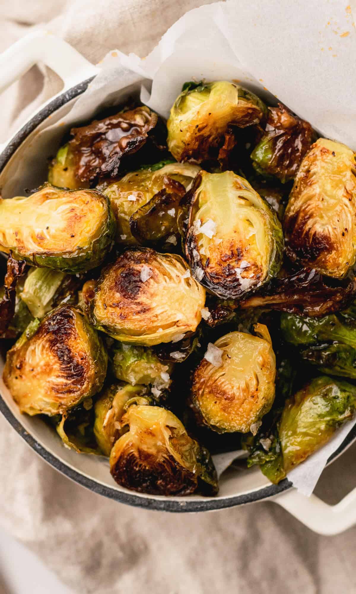A bowl of roasted Brussels sprouts with crispy, caramelized edges, sprinkled with coarse salt. The dish emits a rustic and savory appeal.