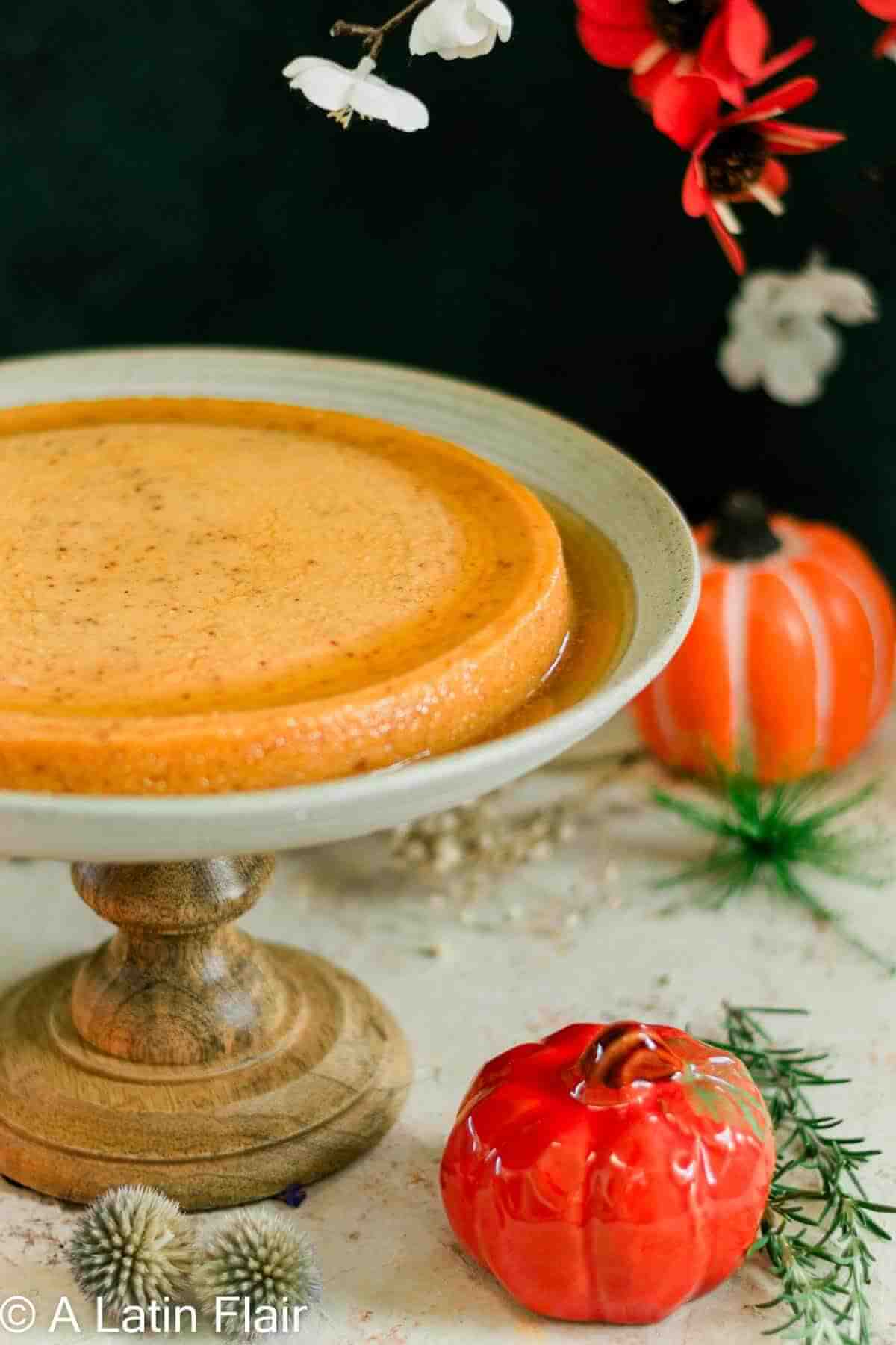 Creamy flan on a wooden stand, surrounded by decorative pumpkins and flowers, exuding a festive and cozy autumn feel.