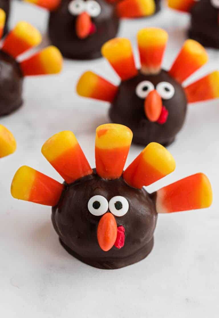 Chocolate turkey truffles with candy corn feathers, googly eyes, and orange beaks on a white surface, creating a festive Thanksgiving treat.