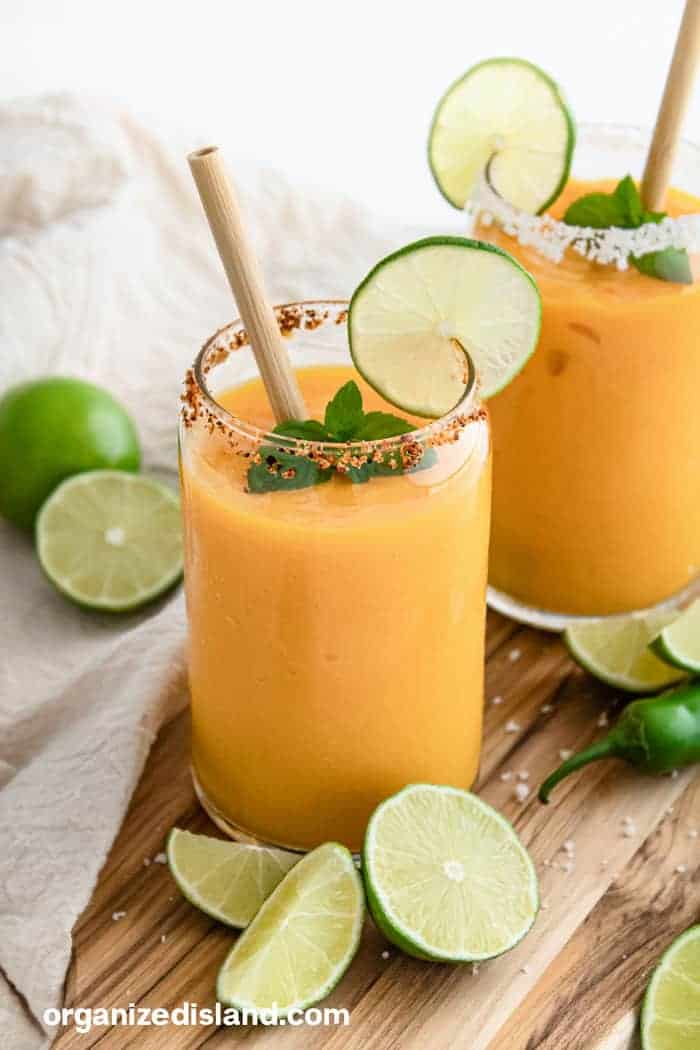 Frozen mango margarita recipe with Tajín rim, lime wheels, and fresh mint in tall glasses served with bamboo straws.