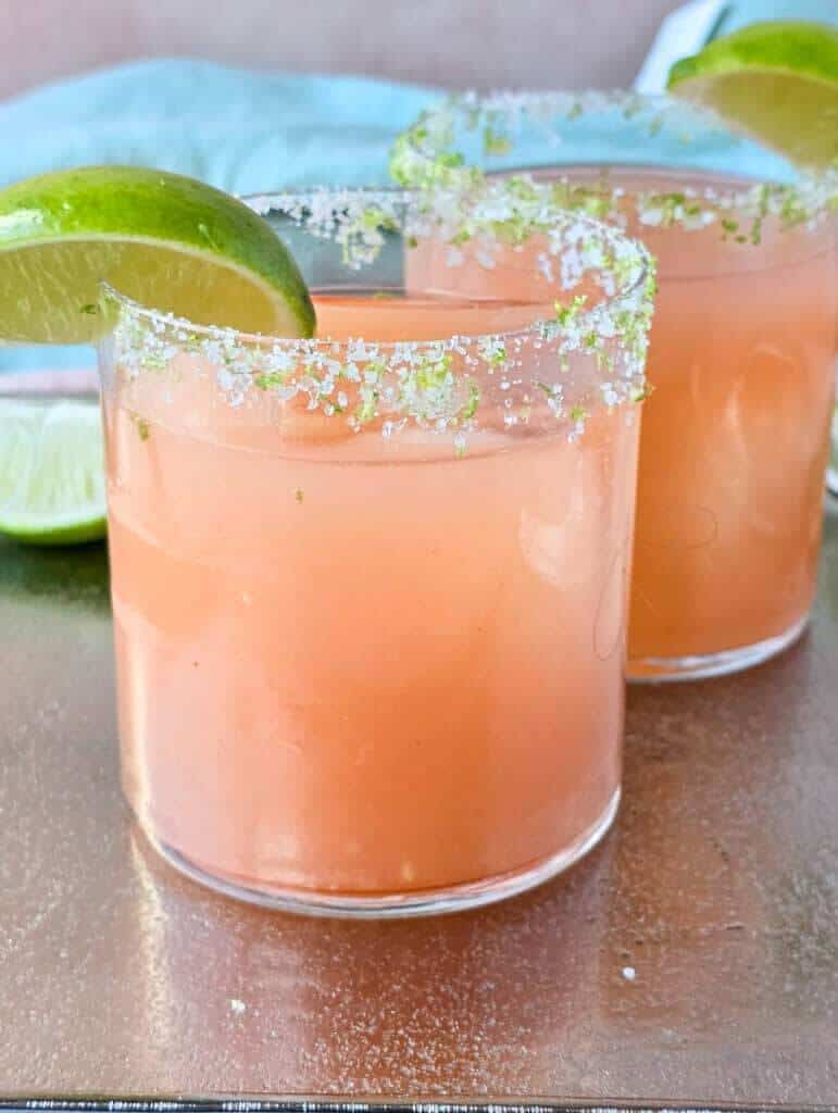 Guava margarita recipe with sugar and lime zest rim, garnished with fresh lime wheel in rocks glass with coral-pink color.