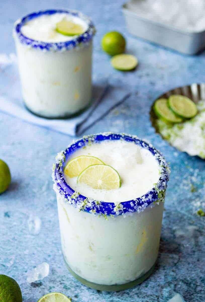 Key lime pie margarita recipe with blue sugar and graham cracker rim, garnished with fresh lime slices and key lime zest.