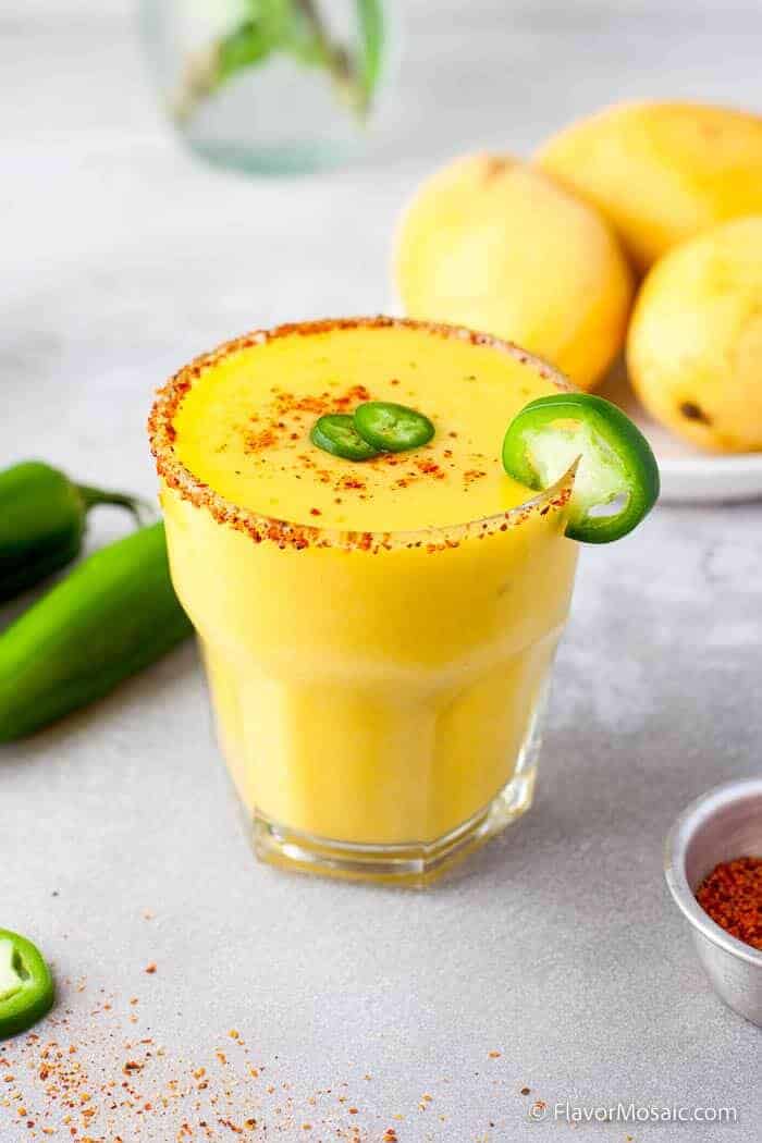 Mango jalapeño margarita recipe with chili salt rim, garnished with fresh jalapeño slices and served with whole mangoes.