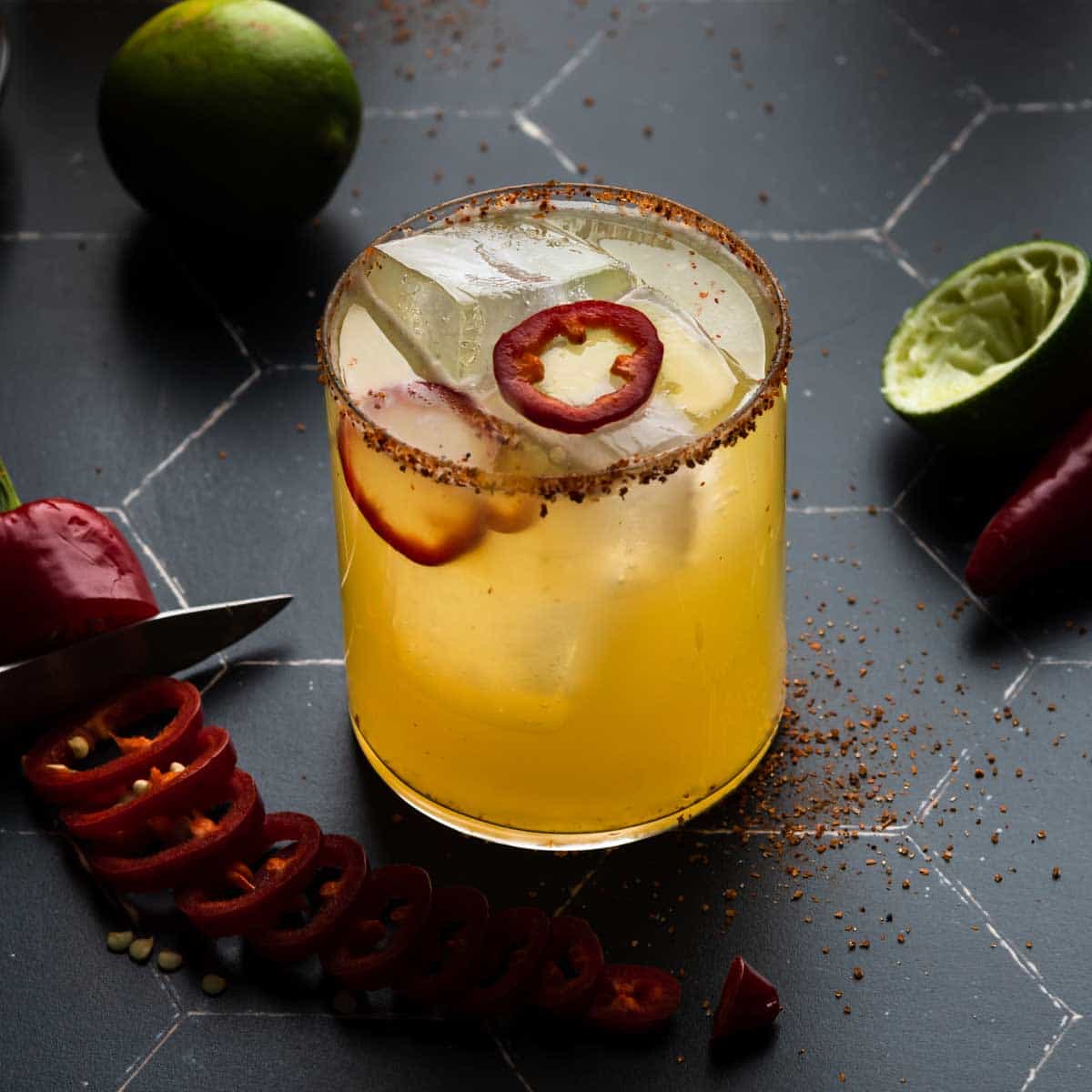 Spicy mezcal margarita recipe with chili salt rim and red pepper garnish, served with fresh lime and sliced red chilies.