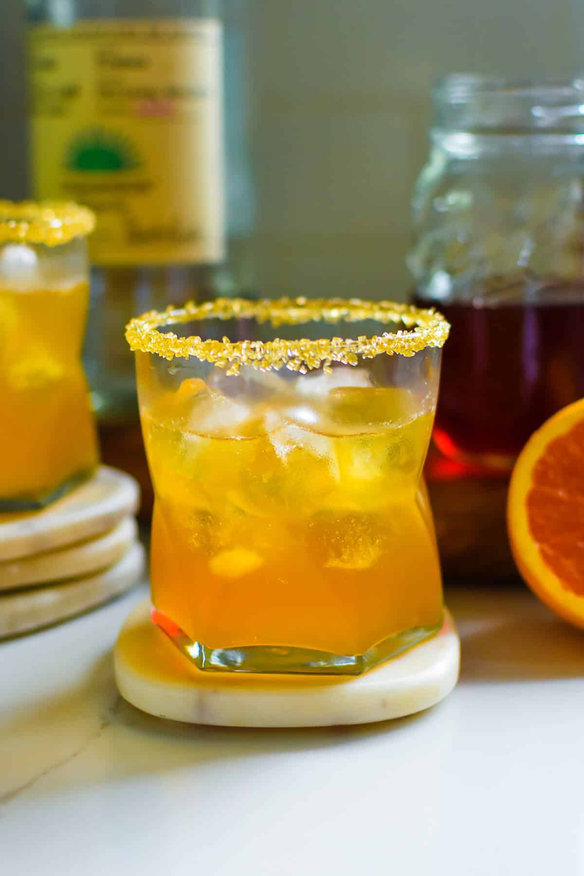 Sweet tea margarita recipe with golden sugar rim served over ice, made with tequila and sweet tea with orange slice.